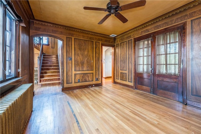 unfurnished room with radiator heating unit, light wood finished floors, stairway, and wood walls