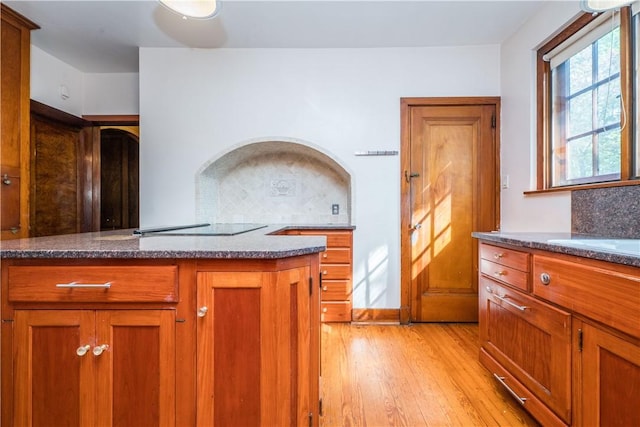 kitchen with brown cabinets, light wood-style flooring, dark stone counters, and tasteful backsplash