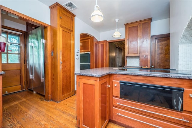 kitchen with visible vents, light wood-style floors, brown cabinets, arched walkways, and backsplash