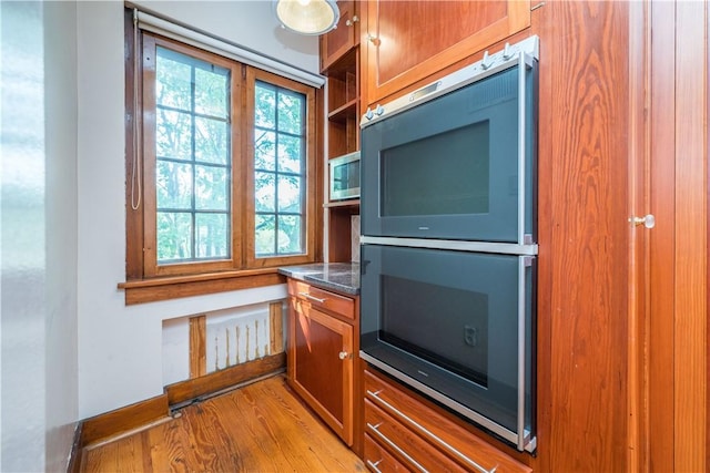 kitchen with dark countertops, brown cabinetry, double oven, and light wood-type flooring