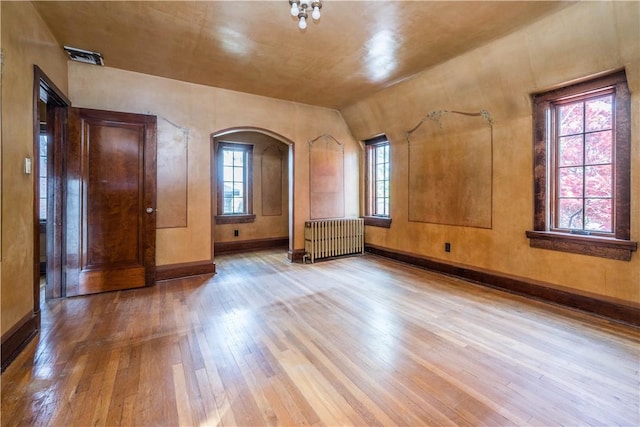 unfurnished room featuring radiator heating unit, arched walkways, baseboards, and wood-type flooring