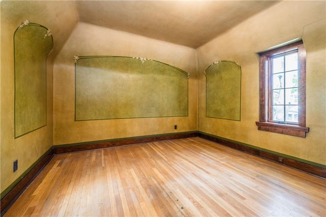 spare room with baseboards, wood-type flooring, and vaulted ceiling