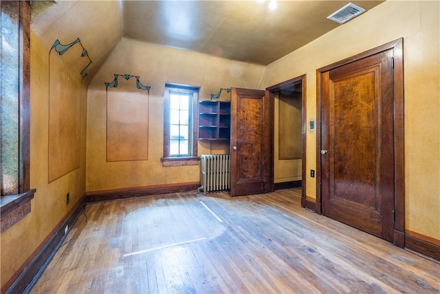 additional living space featuring wood-type flooring, radiator, baseboards, lofted ceiling, and visible vents