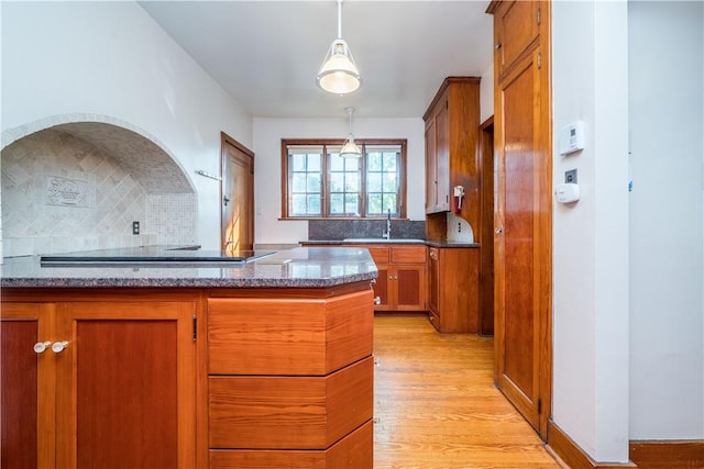 kitchen featuring light wood-style floors, decorative backsplash, black electric stovetop, and brown cabinets