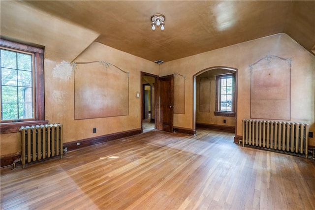 additional living space featuring wood finished floors, arched walkways, radiator heating unit, and a healthy amount of sunlight