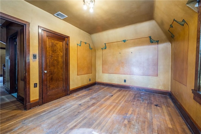 empty room featuring baseboards, visible vents, vaulted ceiling, and hardwood / wood-style floors
