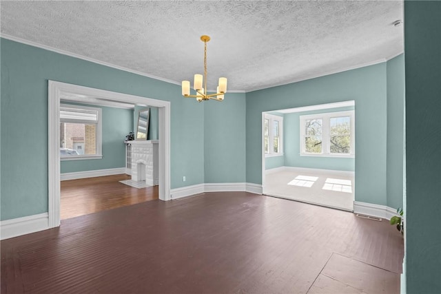 empty room featuring a textured ceiling, wood finished floors, baseboards, a chandelier, and ornamental molding