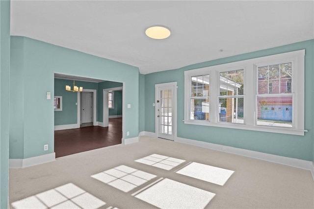 empty room featuring carpet floors, baseboards, and an inviting chandelier