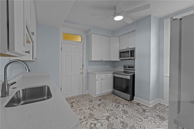 kitchen featuring white cabinets, appliances with stainless steel finishes, a sink, a ceiling fan, and baseboards