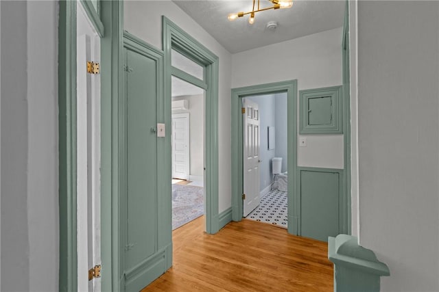 hallway featuring an inviting chandelier, light wood-style floors, and a wall mounted air conditioner