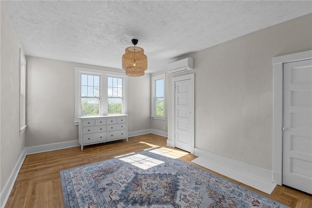 bedroom with an inviting chandelier, a textured ceiling, baseboards, and a wall mounted air conditioner