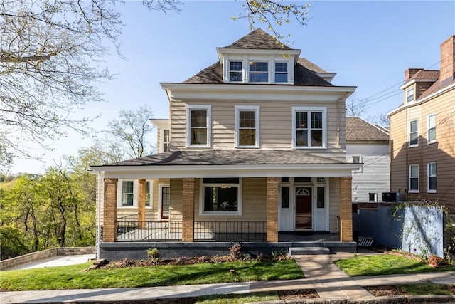 view of front facade featuring a shingled roof, a front lawn, brick siding, cooling unit, and covered porch