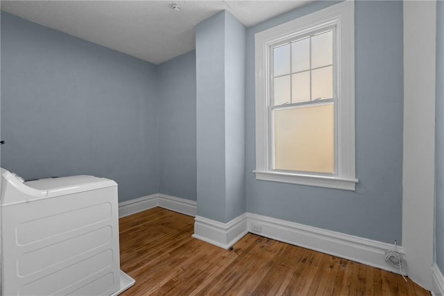 spare room featuring baseboards, washer / dryer, wood finished floors, and a wealth of natural light