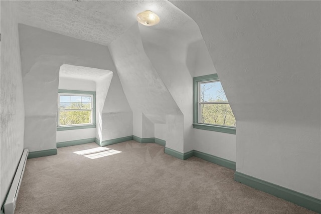 additional living space featuring carpet floors, a baseboard radiator, vaulted ceiling, and a textured ceiling