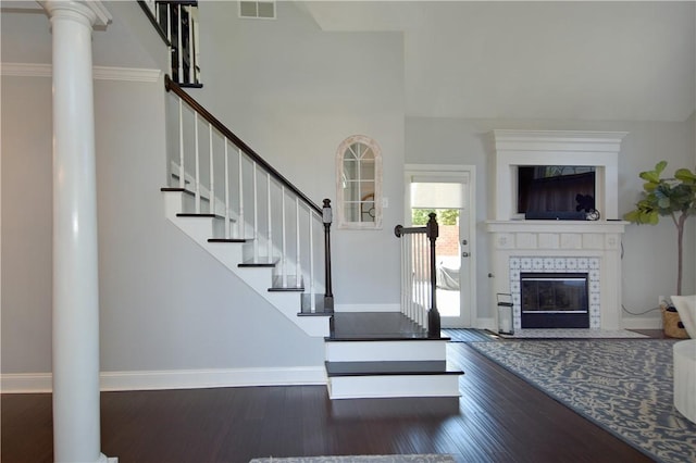 staircase featuring visible vents, a brick fireplace, hardwood / wood-style flooring, baseboards, and ornate columns