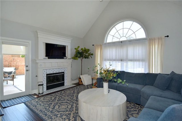 living area with wood finished floors, a wealth of natural light, high vaulted ceiling, and a tile fireplace