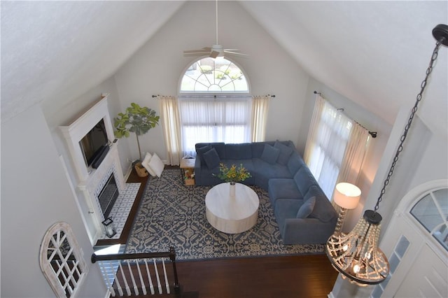 living room featuring a glass covered fireplace, high vaulted ceiling, ceiling fan, and wood finished floors
