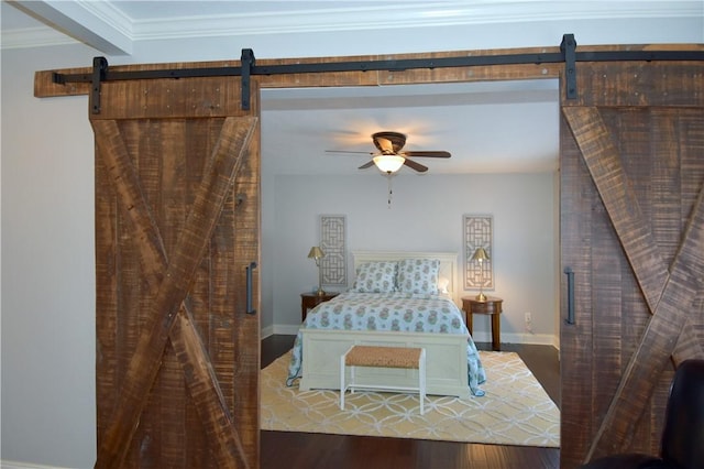 bedroom featuring ceiling fan, a barn door, baseboards, wood finished floors, and ornamental molding