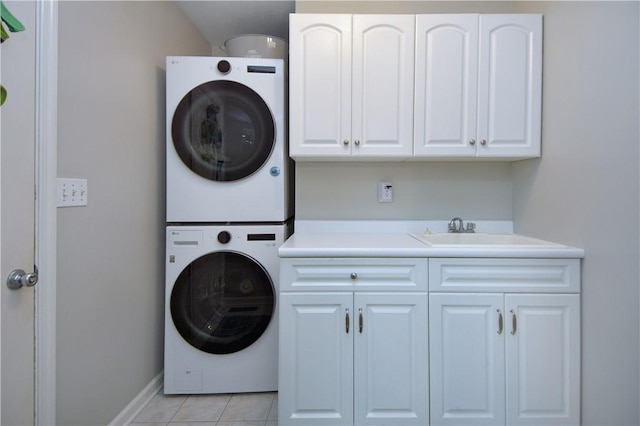 laundry room featuring light tile patterned flooring, stacked washer / dryer, baseboards, a sink, and cabinet space