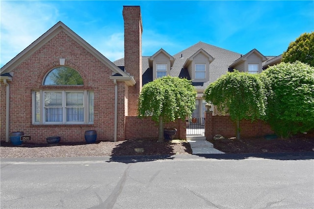 view of front of home featuring brick siding, fence, and a chimney