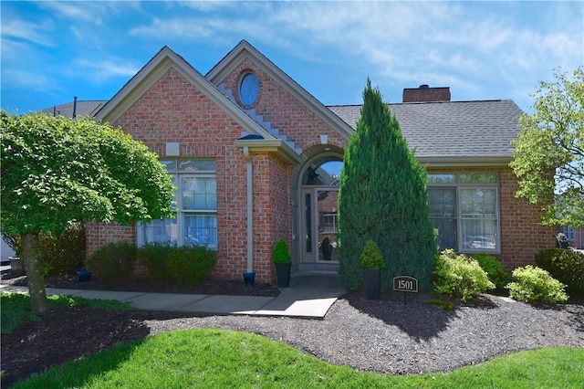 view of front of house with brick siding, a chimney, and a shingled roof