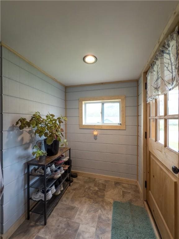 entryway with wooden walls, baseboards, and stone finish floor