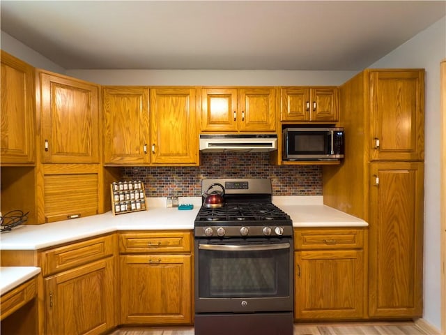 kitchen featuring brown cabinetry, light countertops, under cabinet range hood, and stainless steel appliances
