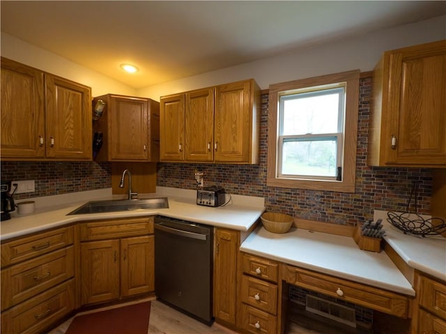 kitchen featuring a sink, light countertops, brown cabinetry, decorative backsplash, and dishwashing machine