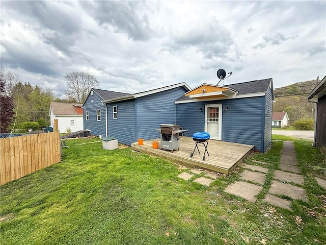 rear view of property with a yard, a deck, fence, and roof with shingles