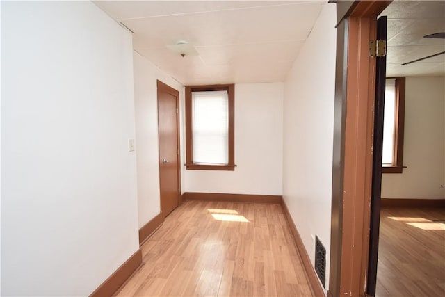 hallway with baseboards, visible vents, and light wood finished floors