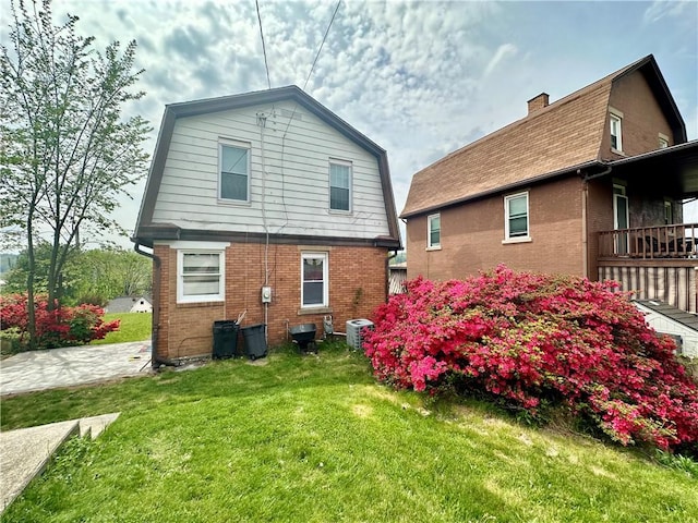 rear view of property featuring brick siding, a gambrel roof, a lawn, and central AC unit
