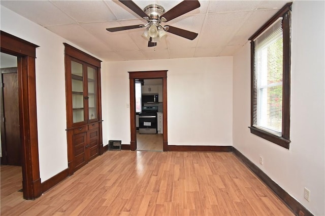 empty room with baseboards, a drop ceiling, ceiling fan, and light wood-style floors