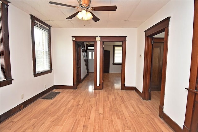 spare room featuring baseboards, ceiling fan, light wood-style flooring, and visible vents