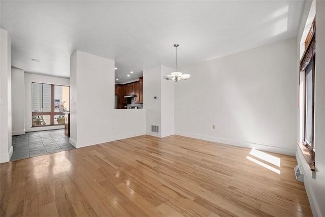 unfurnished living room with baseboards, visible vents, light wood-type flooring, and a chandelier