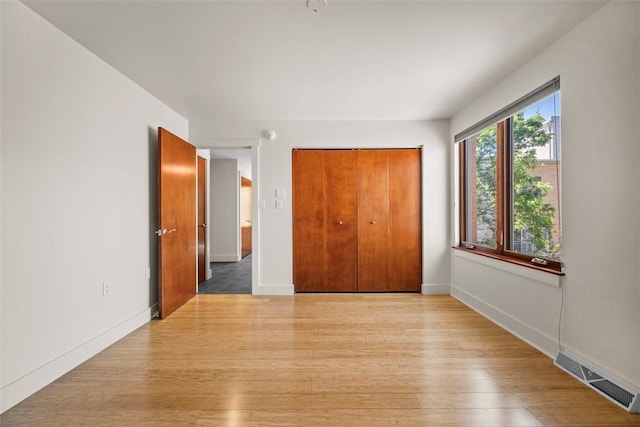 unfurnished bedroom featuring baseboards, a closet, light wood-style flooring, and visible vents