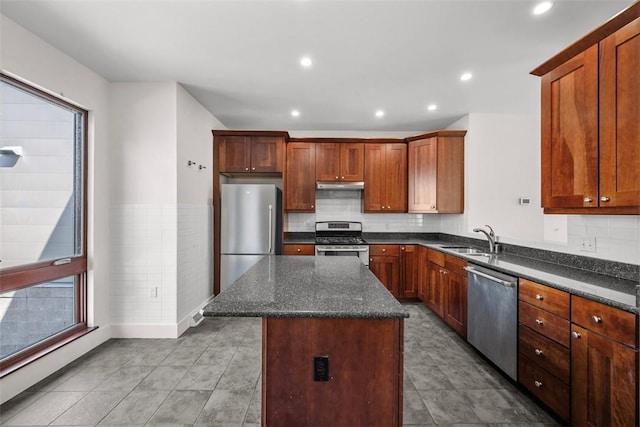 kitchen with under cabinet range hood, appliances with stainless steel finishes, dark stone counters, and a center island