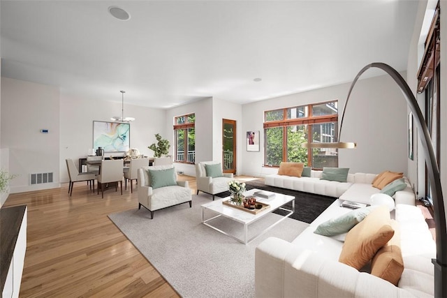 living area featuring a notable chandelier, visible vents, a wealth of natural light, and light wood-style floors