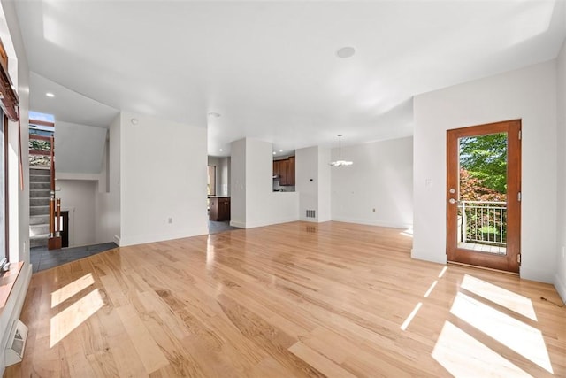unfurnished living room featuring visible vents, light wood-style flooring, baseboards, and a chandelier