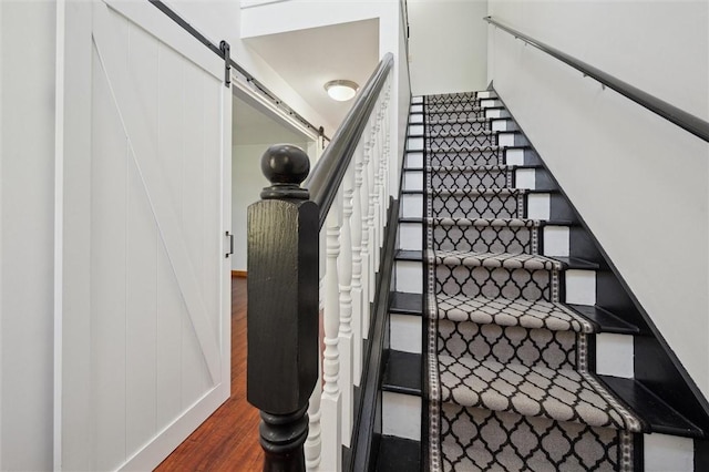 staircase with a barn door and wood finished floors