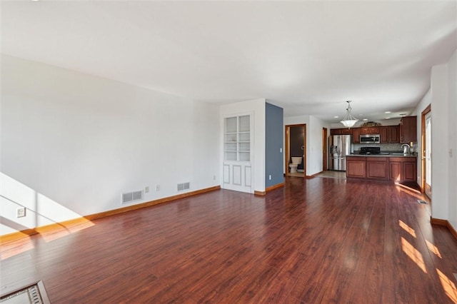 unfurnished living room with a sink, baseboards, visible vents, and dark wood finished floors