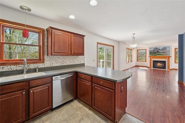 kitchen featuring stainless steel dishwasher, a peninsula, tasteful backsplash, a sink, and hanging light fixtures