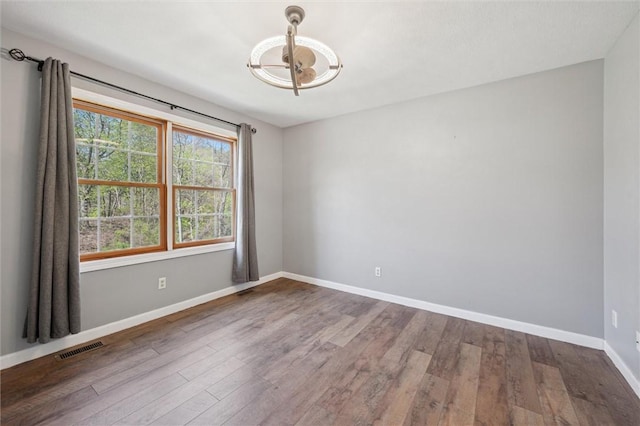 spare room with visible vents, baseboards, wood finished floors, and an inviting chandelier