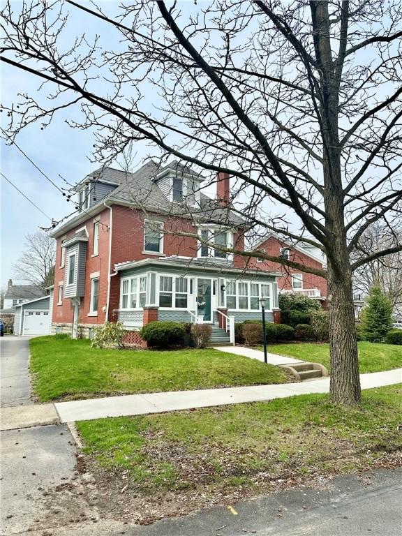 traditional style home with entry steps, a chimney, a front lawn, and brick siding