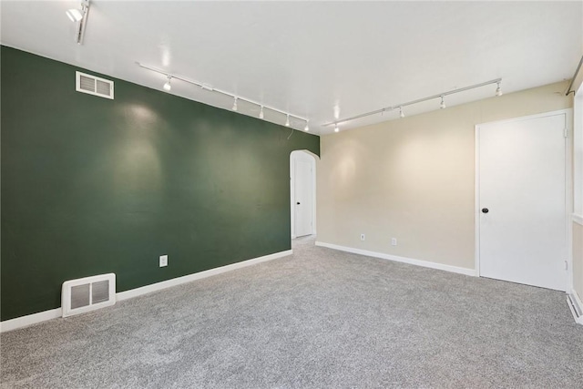 carpeted spare room with track lighting, baseboards, arched walkways, and visible vents