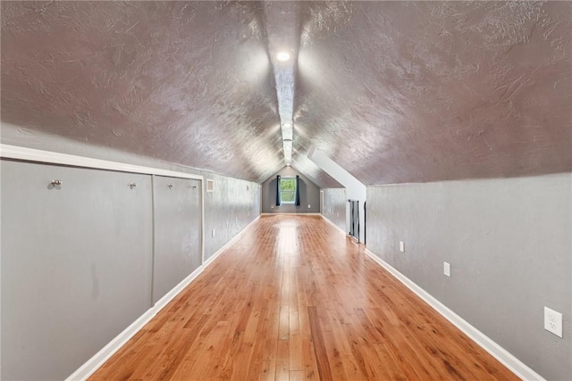 additional living space featuring baseboards, a textured ceiling, vaulted ceiling, and hardwood / wood-style flooring