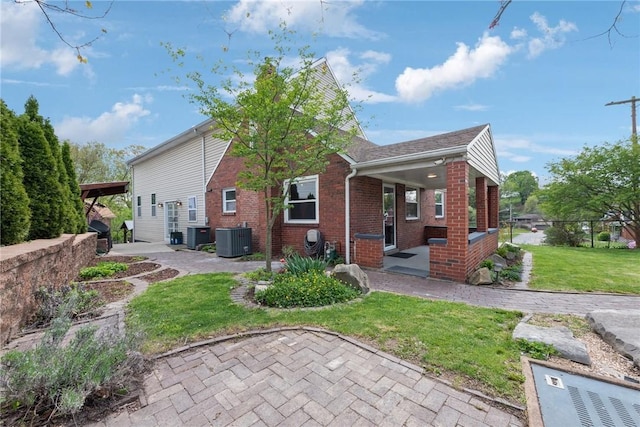 back of house with brick siding, central AC, a yard, and a porch