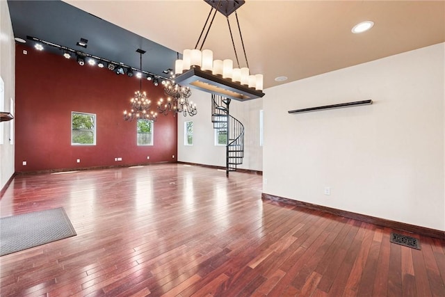 unfurnished living room featuring visible vents, an inviting chandelier, stairs, hardwood / wood-style floors, and baseboards