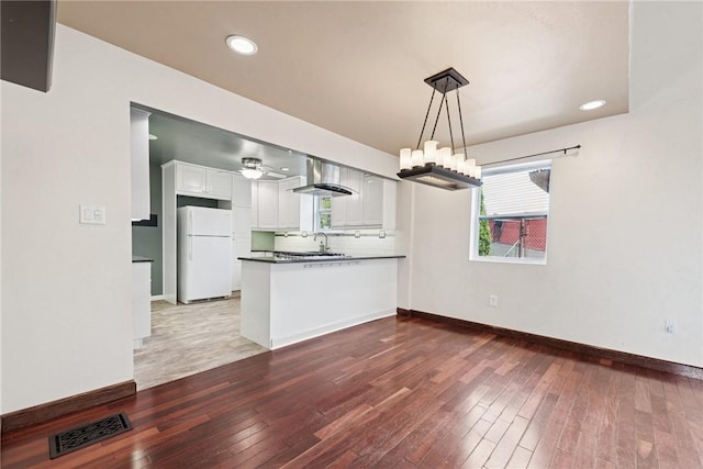kitchen featuring wall chimney range hood, wood-type flooring, freestanding refrigerator, a peninsula, and visible vents