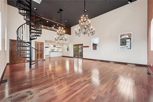 unfurnished living room with visible vents, wood finished floors, stairway, an inviting chandelier, and a high ceiling