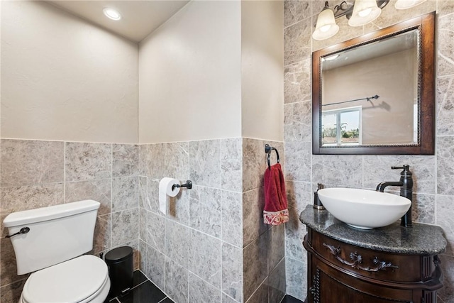 bathroom featuring toilet, tile walls, wainscoting, and vanity